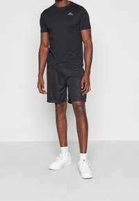 Černé bavlněné tričko s krátkým rukávem a logem na hrudi, spárované s odpovídajícími černými šortkami a bílými teniskami.