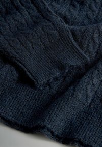 Námornícky modrý pletený materiál s jemným, textúrovaným povrchom a rebrovanými manžetami. Materiál vyzerá nadýchaný a teplý.