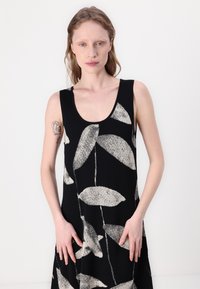 Svart ärmlös klänning med ett stort mönster av krämfärgade blad. Tillverkad av ett texturerat tyg, har den en rundad halsringning och en avslappnad passform.