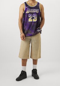 Fioletowy strój koszykarski z napisem "Lakers" i numerem "23", w połączeniu z beżowymi szortami do kolan i czarnymi trampkami.