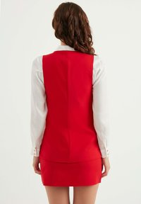Röd klänning med en figurnära bodice och kort kjol. Långärmad vit skjorta under, med knappdekorationer på ärmsluten.