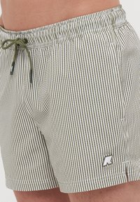 Costumi da bagno a righe verdi e bianche, dotati di vita elastica con cordino, tasche laterali e un piccolo logo dettagliato sull'orlo.