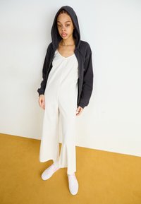 Mono blanco de pernera ancha con un escote profundo, combinado con una sudadera oscura y zapatillas de cuadros rosas. Tejido suave y corte relajado.