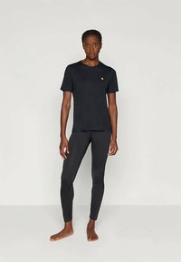 Μαύρο κοντομάνικο μπλουζάκι με ένα μικρό κίτρινο λογότυπο και στενές μαύρες κολάν, και τα δύο φτιαγμένα από ένα λείο, ελαστικό ύφασμα.