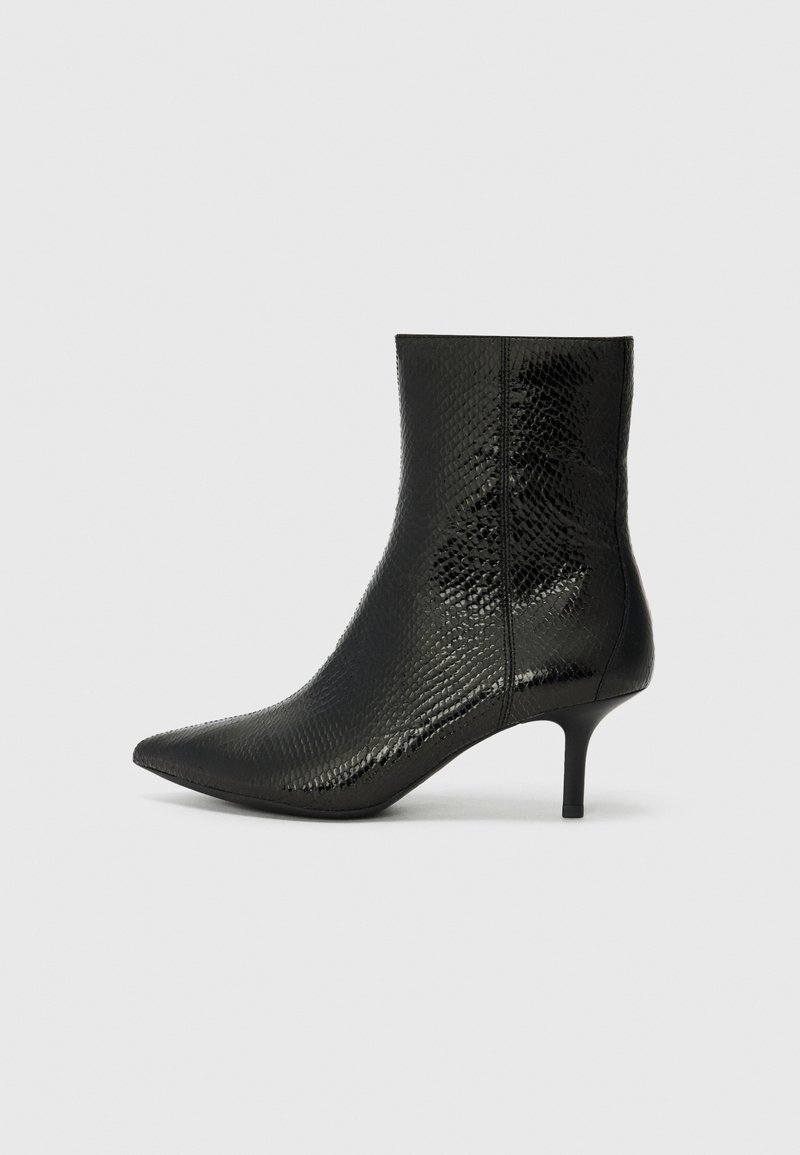 Botte mi-mollet en cuir noir avec bout pointu, motif peau de serpent texturé et talon kitten fin sur un fond gris clair uni.