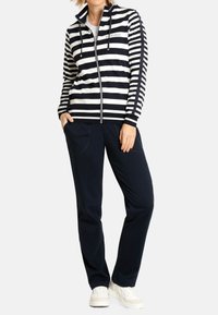 Haut à capuche zippé rayé bleu marine et blanc avec une coupe décontractée, associé à un pantalon bleu marine foncé et des baskets blanches. Caractéristiques : deux poches avant.