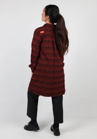 Chemise rouge et noire à motifs, ornée de designs géométriques et d'accents ronds. Texture douce, fermeture à boutons et poches latérales.