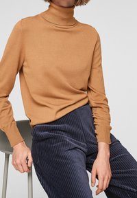 Hnědý rolák s ribpoovaným texturou a přiléhavými rukávy, spárovaný s námořnickými kordovým kalhotami se svislými pruhy.