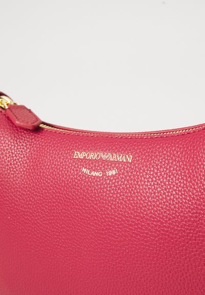 Red textured leather zip pouch with gold Emporio Armani logo and "Milano 1981" text embossed below zipper.