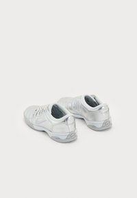 Zapatillas deportivas blancas fabricadas con materiales sintéticos, con un cuello acolchado, suelas texturizadas y acentos reflectantes en el talón y los laterales.