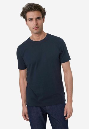 Marineblaue Baumwoll-T-Shirt mit kurzen Ärmeln und Rundhalsausschnitt, locker sitzend und mit glatter Textur. Getragen mit dunklen Jeans.