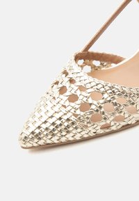 Χαλυβδόχρυσο μεταλλικό παντόφλα με μύτη σε σχήμα μυτερό, πλεγμένο δέρμα με ανοιχτό σχεδιασμό πλέγματος και λεπτό λουράκι στον αστράγαλο.