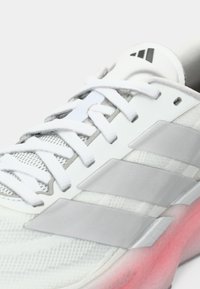 Κοντινό πλάνο λευκού αθλητικού παπουτσιού με γκρι ρίγες, λευκά κορδόνια, επάνω μέρος από δίχτυ και μεσαία σόλα με ροζ λεπτομέρειες.