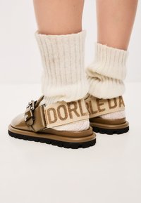 Sandali platform beige con una finitura lucida, dettaglio con fibbia e calze di maglia crema con una texture a coste piegate per rivelare i sandali.