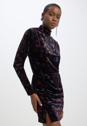 Abito di velluto nero con motivi floreali e paisley, colletto alto, maniche lunghe, dettagli arricciati in vita e uno spacco laterale.