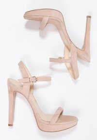Beiga mockaskinnsandaler med hög klack, stängd bak, öppen tå och ankelsnören. Har ett guldspänne och en plattformdesign.