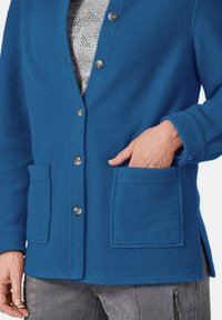 Blauwe cardigan van textuurmateriaal met een V-hals, knoopsluiting, twee voorkruiszakken en zijsplitten voor gemak van beweging.