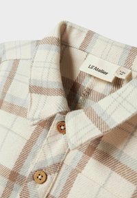 Camicia a quadri beige e marrone con una texture morbida, dotata di colletto, bottoni in legno e un'etichetta tessuta con "Lil'Atelier."