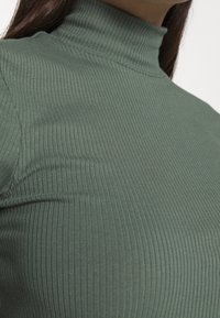 Rybkovaný rolák vyrobený z elastické tkaniny v olivově zelené barvě. Detailní pohled zdůrazňující texturu a přiléhavý design.