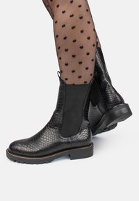 Botas de tobillo negras con un acabado de piel de serpiente texturizada, paneles laterales elásticos y una suela de goma con un acento de costura en contraste.