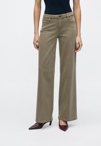 Zöld, bőszárú farmernadrág, elülső zsebekkel, cipzáros zárral és gombos rögzítéssel. Párosítva hegyes orrú, bordó magassarkúval.