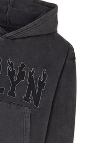 Sudadera gris con capucha ajustable, que presenta un gran logo bordado en negro que dice "BROOKLYN". El material parece suave y tiene una textura ligeramente desgastada.