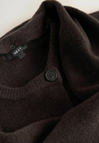 Dunkelbrauner gestrickter Pullover mit V-Ausschnitt, ausgestattet mit einem gerippten Kragen und einem schwarzen Knopf. Das Etikett trägt die Aufschrift "NEXT". Weicher, strukturierter Stoff.