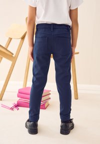 Pantaloni blu navy con un design aderente, dotati di una vita posteriore, due tasche posteriori e gambe affusolate, abbinati a scarpe nere.