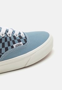 Lichtblauwe canvas sneaker met een zwart- en blauwgebroken patroon, witte veters en een gestructureerde witte rubberen zool.
