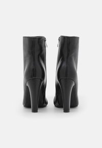 Botas de cuero negro hasta el tobillo con tacón alto, con una textura suave, cremalleras traseras y detalles de costura vertical.