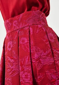 Punane seelik, millel on tekstureeritud lillemuster tumedamatest punastest ja roosadest tooni. Omab voldikesi ja sobivat vööd keeruka detailiga.