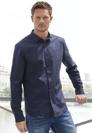 Marineblaue Langarmbluse mit einem Button-Down-Kragen, glattem Stoff, klassischem Schnitt und vorderem Knopfverschluss, kombiniert mit hellblauen Jeans.