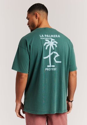 Groen katoenen T-shirt met een witte grafische print van een palmboom en de tekst "LA PALMERA BEACHCLUB PROTEST" op de achterkant. Korte mouwen.