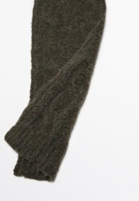 Jambières tricotées vert foncé en tissu texturé avec des poignets côtelés, présentant une apparence douce et duveteuse.