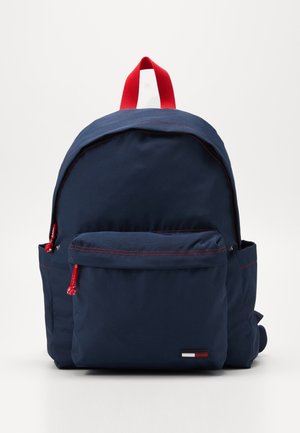 Marineblauer Rucksack mit Vordertasche, roten Reißverschlussanhängern, rotem Trageschlaufe und kleinem rot-weiß-blauem Logo auf der Tasche.