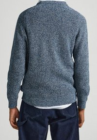 Texturovaný modrý svetr s kulatým výstřihem a žebrovanými manžetami. Obsahuje melírovaný úplet. Nalezen pod ním viditelná bílá košile.