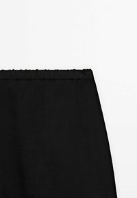 Musta joustava vyötärönauha virtaavien housujen yläosassa. Kangas on sileäpintainen ja mattapintainen. Ei näkyviä kuvioita tai korostuksia.