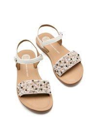 Sandalias planas con una correa ajustable blanca, que presentan una amplia banda de cuentas en tonos rosa y crema, y una suela marrón texturizada.