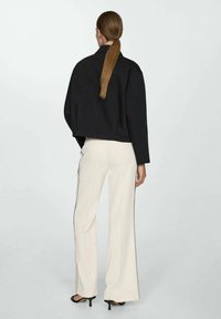 Zwarte cropped jack, crèmekleurige wijde broek met zijstrepen en hoge hakken sandalen. Soepele texturen en een minimalistisch ontwerp. Achteraanzicht.