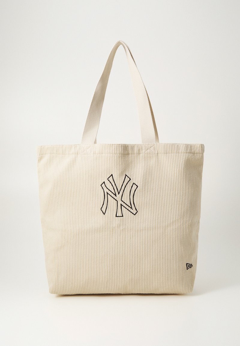 Μπεζ τσάντα χειρός από κοτλέ με μαύρο κεντημένο λογότυπο, μακριές υφασμάτινες λαβές και υφή, με κάθετες ραβδωτές γραμμές.