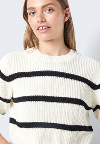 Strikkegenser med rund hals, har horisontale svarte striper på en off-white bakgrunn, lett strukturert stoff, korte ermer.