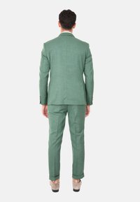 Completo verde con un tessuto texturizzato, caratterizzato da un giubbotto a un bottone e pantaloni, entrambi tagliati con una vestibilità slim e polsini arrotolati.