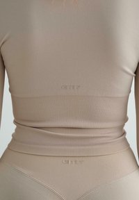 Beige ribbed long-sleeve crop top with a fitted design. Features a smooth texture and a logo at the hem. Styled with matching high-waisted bottoms.