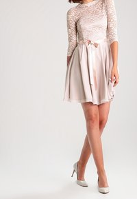 Krátké růžové šaty s krajkovým tělem a tříčtvrtečním rukávem, se širokou chiffonovou sukní, zakončené saténovou mašlí v pase.