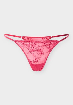 Tanga en dentelle rouge transparente avec broderie florale et fines bretelles latérales réglables sur un fond clair uni.