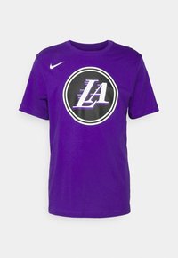 T-shirt en coton violet avec un logo circulaire noir portant "LA" en blanc et violet, et un petit swoosh Nike blanc sur l'épaule gauche.
