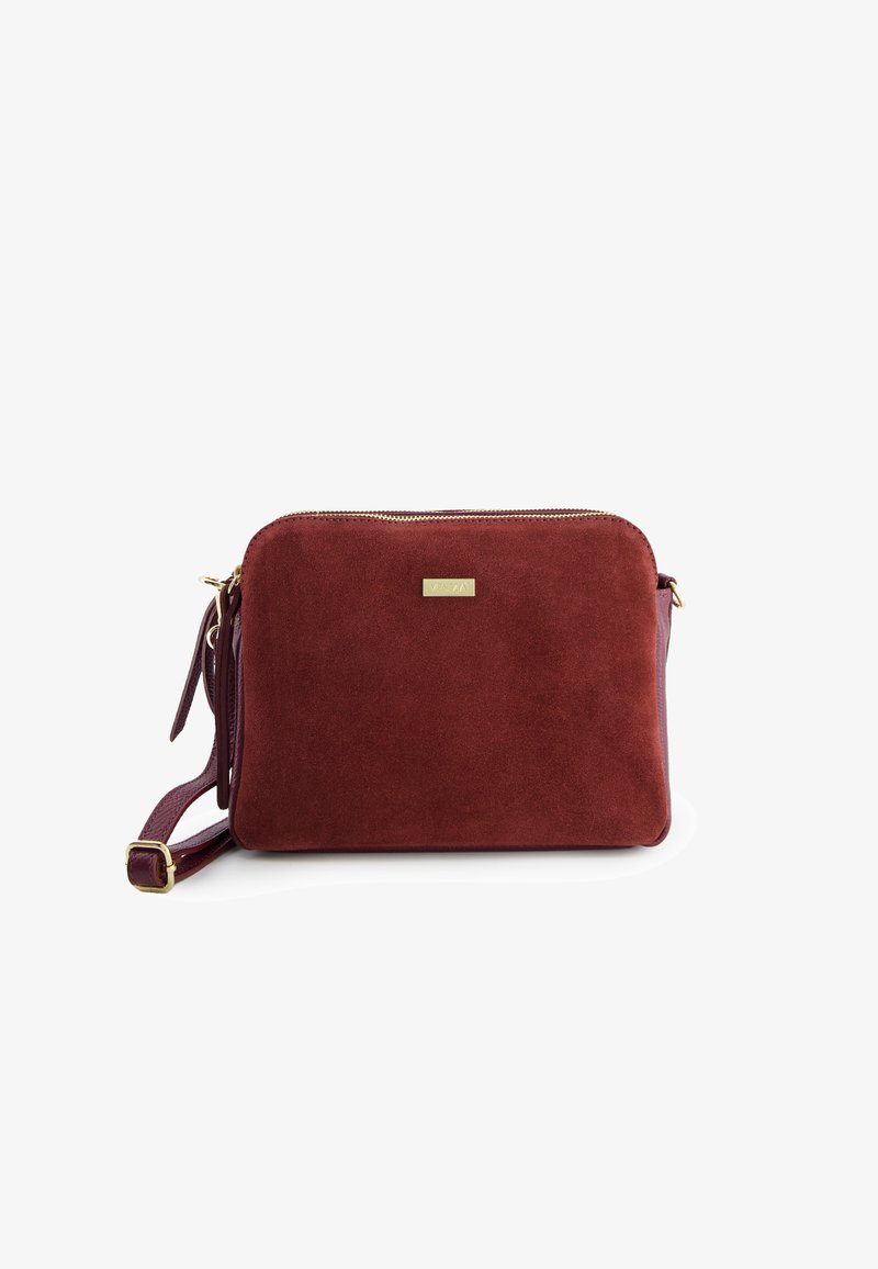 Burgundy suede crossbody bag with a smooth texture, gold zipper, and metallic brand plate; features an adjustable strap.