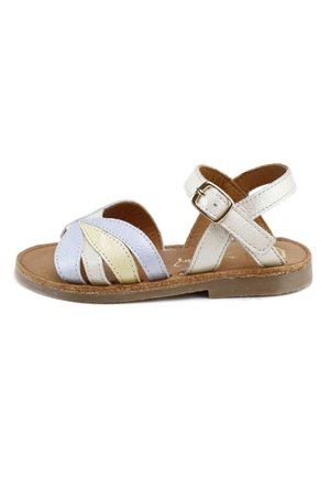 Sandalia infantil de cuero blanco con tiras en forma de hoja amarillas y azules, correa en el tobillo con hebilla y suela marrón sobre fondo blanco.