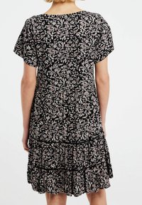 Musta kukallinen mekko lyhyillä hihoilla, jossa on kerroksellinen röyhelöhelma ja pieniä lehtiä pinkin ja vihreän sävyissä.