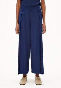Marineblauwe wijde broek van zacht materiaal met een elastische tailleband en voorplooien. Soepele textuur met een vloeiende silhouet.